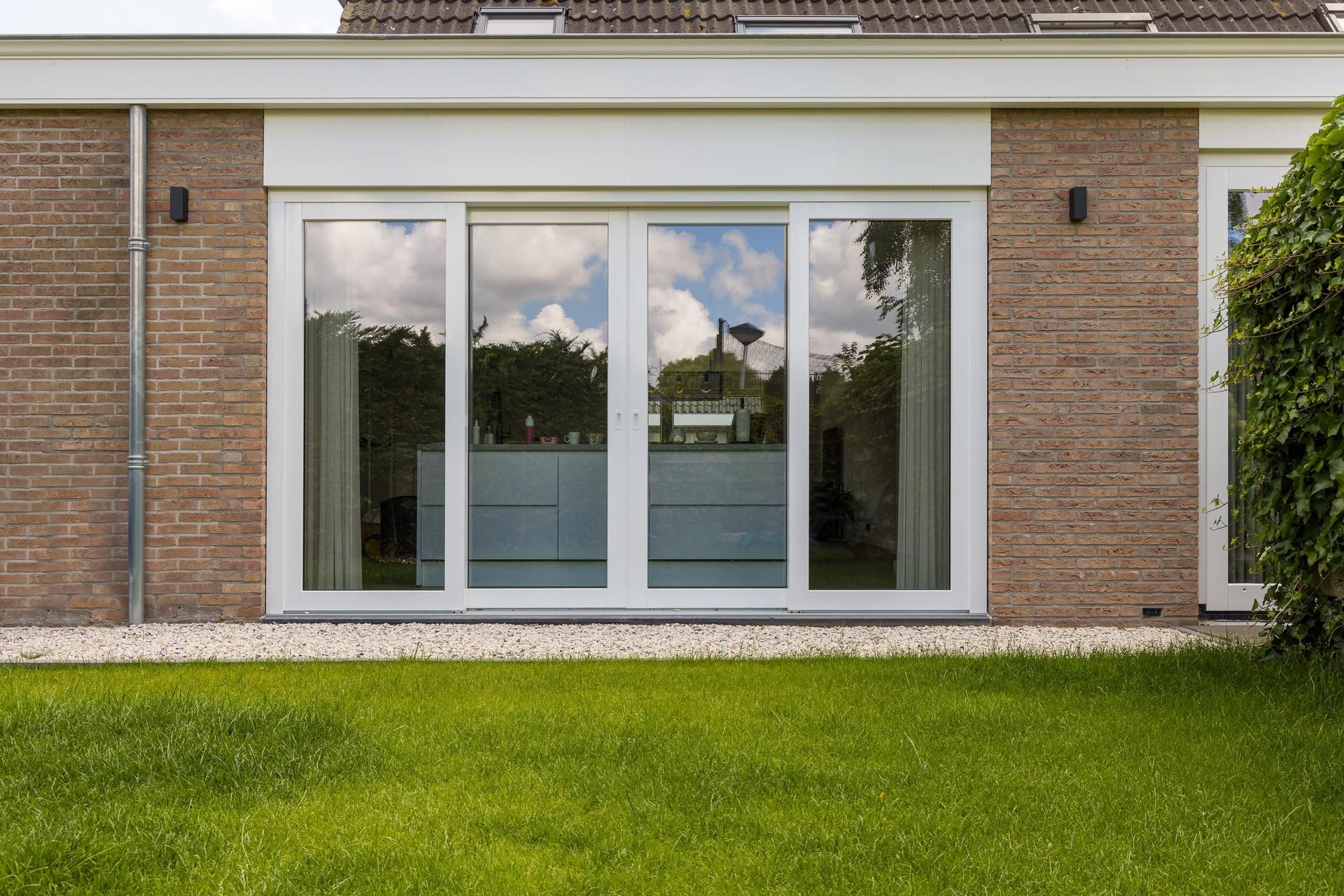 High-tech Knipping kozijnen voor energiezuinige renovatie Moderne gevel met antracietkleurige kozijnen en glazen schuifdeuren op een zonnige dag.