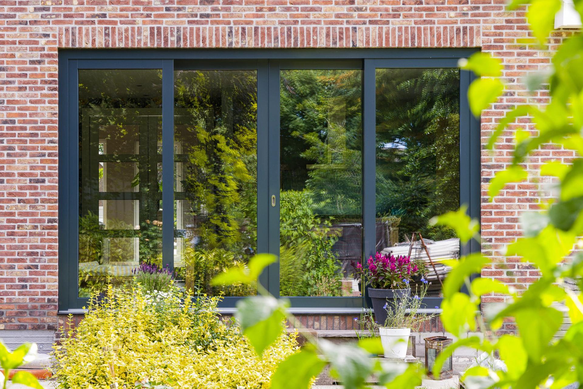 Knipping deuren in renovatieproject Moderne witte kunststof deur met glazen panelen en groene planten op de voorgrond bij een woningingang.