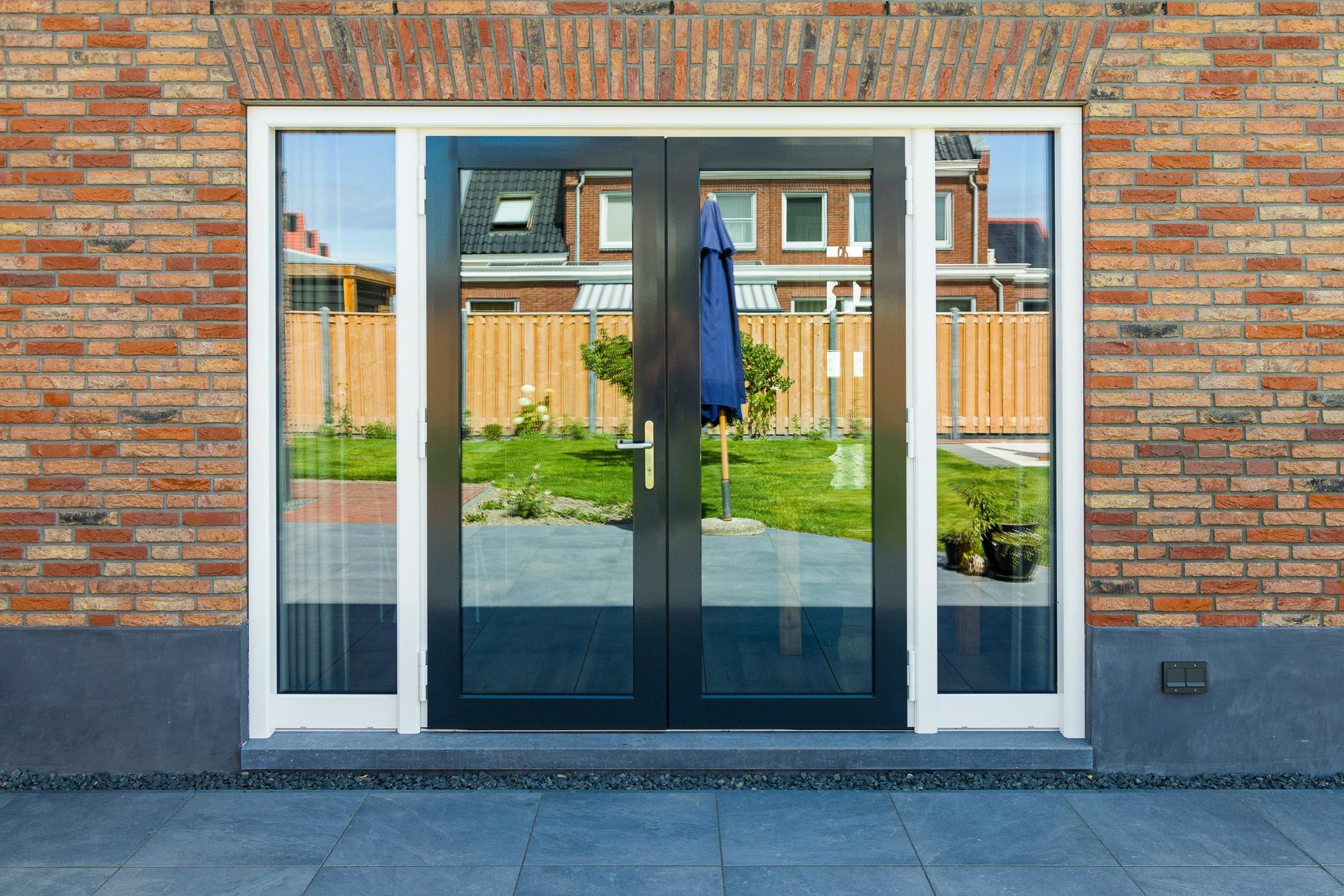 Moderne, witte kunststof kozijnen op een huis met grijze bakstenen, met helderblauwe lucht op de achtergrond.