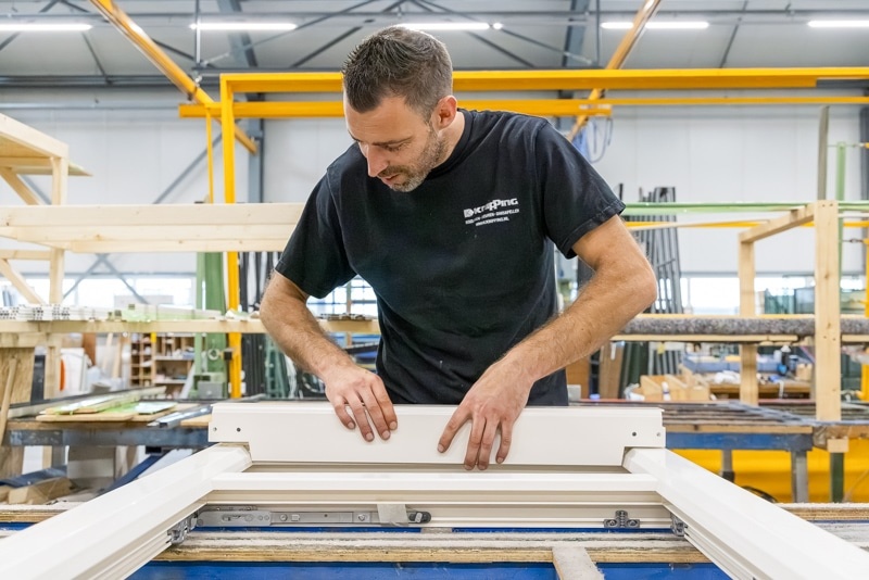 Moderne glazen schuifpui met wit frame, geopend naar een zonnige tuin met groene planten en blauwe lucht.